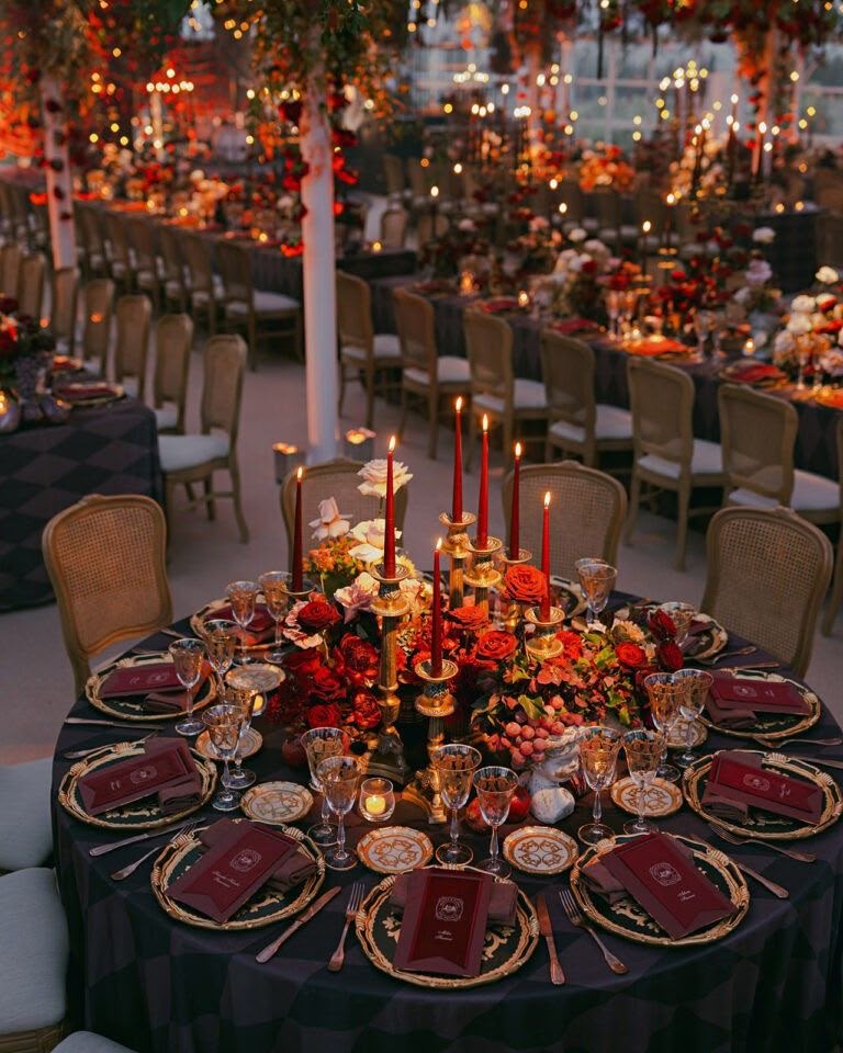 Round tables set with tall red candles and gold chargers at dusk